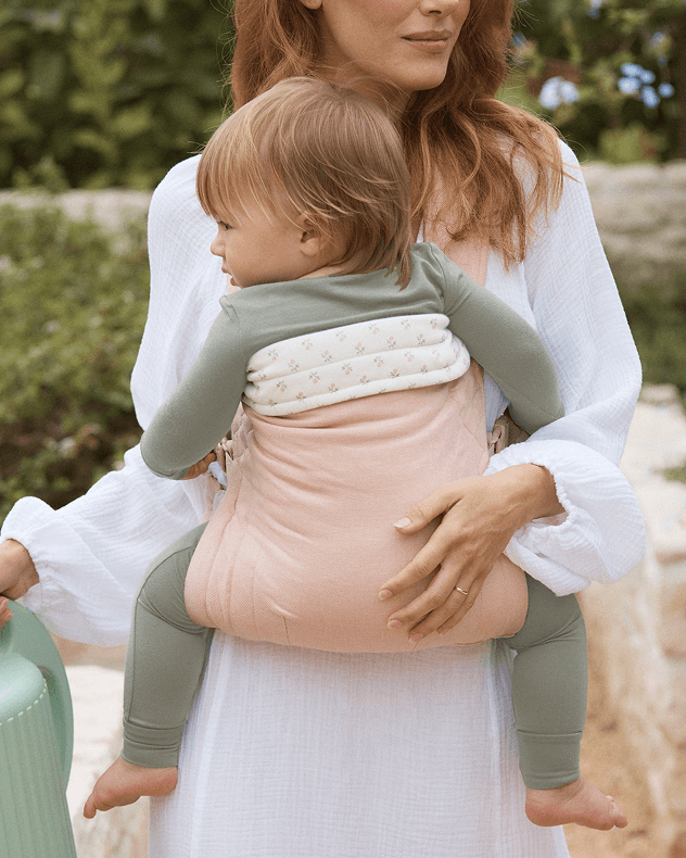 Mom holding a toddler in a pink stuctured buckle carrier outdoors while walking