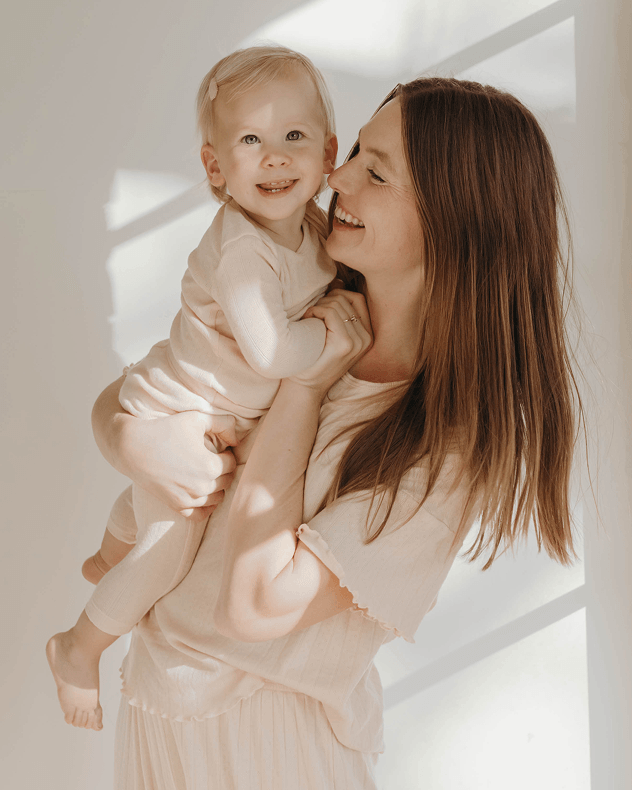 Mom holding baby indoors while wearing matching pointelle sleep sets while both smiling