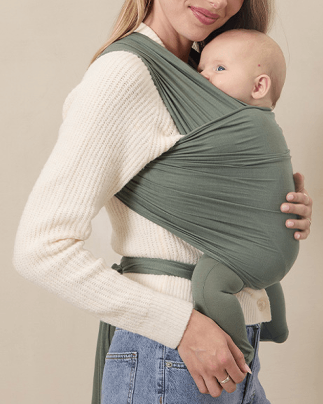 Close up of mom holding baby wearing a green baby wrap carrier against tan background