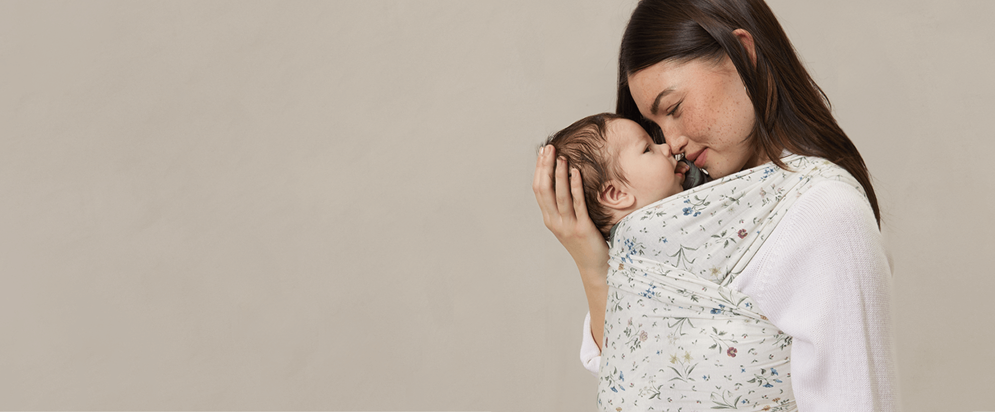 Woman holding a baby in a floral baby carrier against a beige background