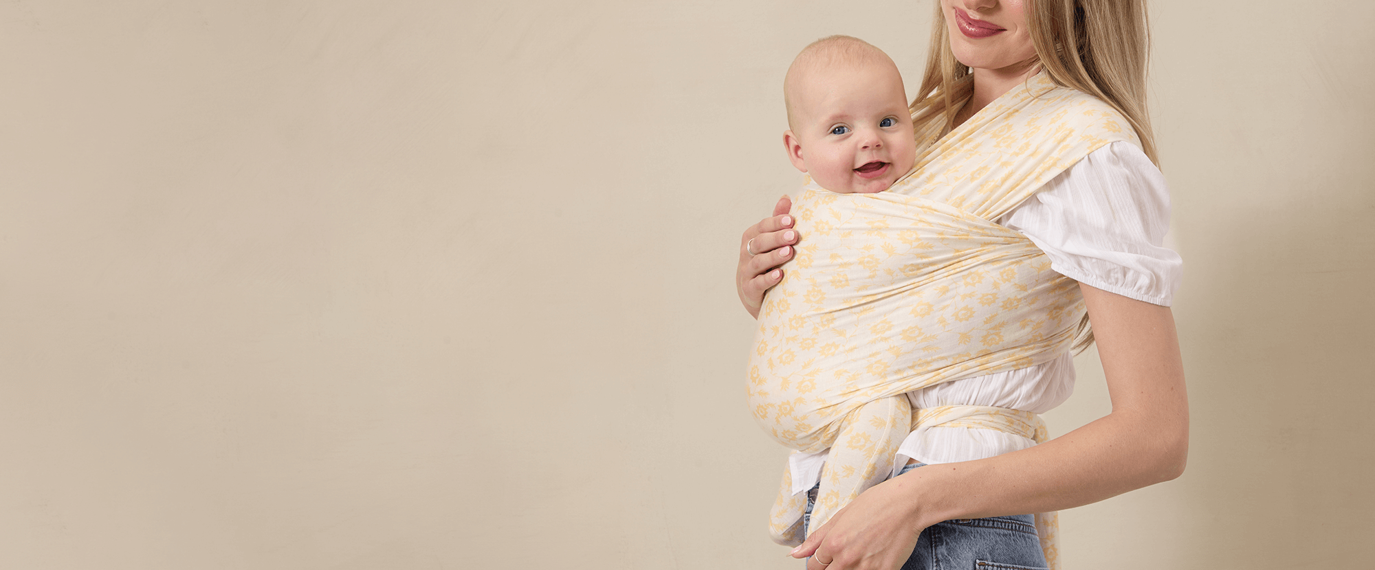 Smiling baby carried heart-to-heart in the Solly Baby Wrap in Buttercup print. The lightweight, breathable fabric offers comfort and support for sunny day adventures.