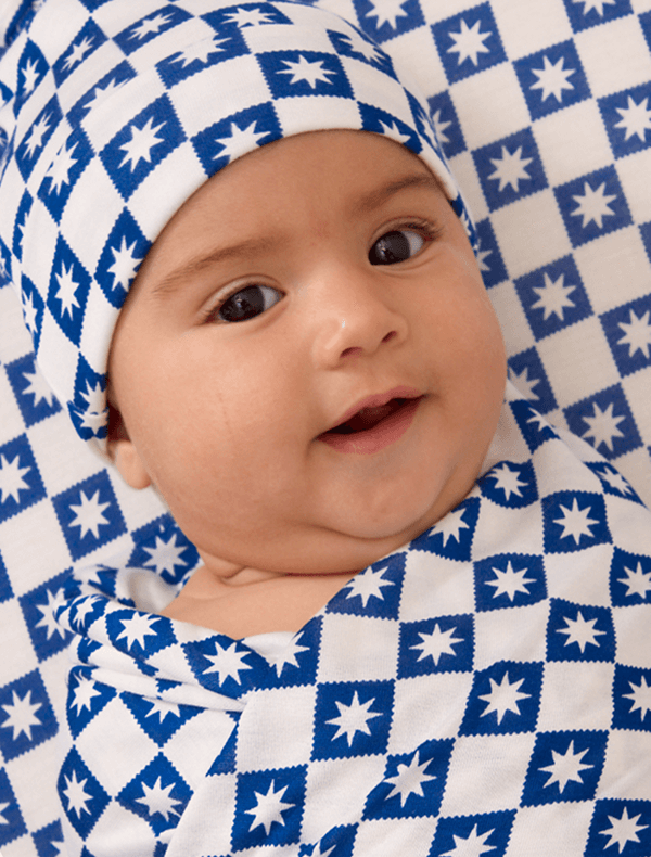 Baby smiling in blue checkered and starred swaddle + hat set.