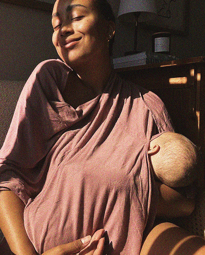 Woman wearing a pink baby wrap holding a baby indoors.