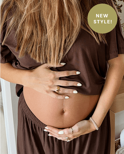 A pregnant woman wearing a brown maternity top and matching bottoms, holding her baby bump. She has long blonde hair, white manicured nails, and is wearing rings. There is a circle on the pictures that calls out "New Style!"