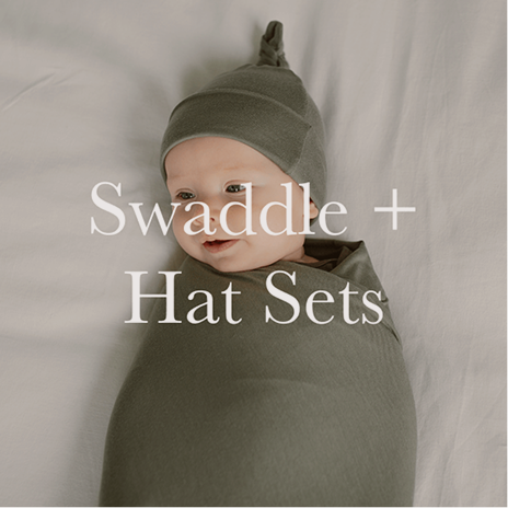 Baby swaddled in a green swaddle with matching hat on a plain background, with text 'Swaddle + Hat Sets'.