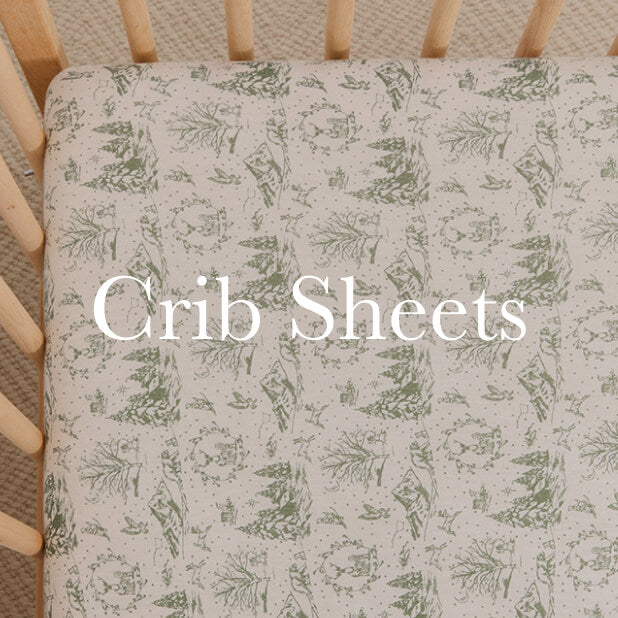 Cream crib sheet with green winter toile pattern on a natural wood crib. Shop Crib Sheets. 