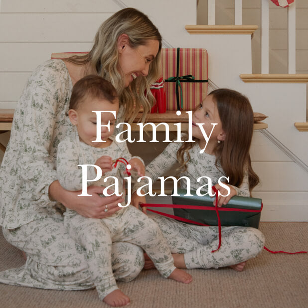 Mom and two children in matching cream and green winter toile pajamas sitting near holiday gifts on a staircase. Shop Family Pajamas. 