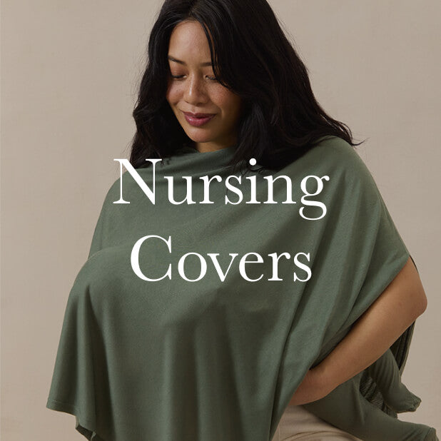 Mom smiling while using a basil green nursing cover, seated against a soft neutral background. Shop Nursing Covers. 