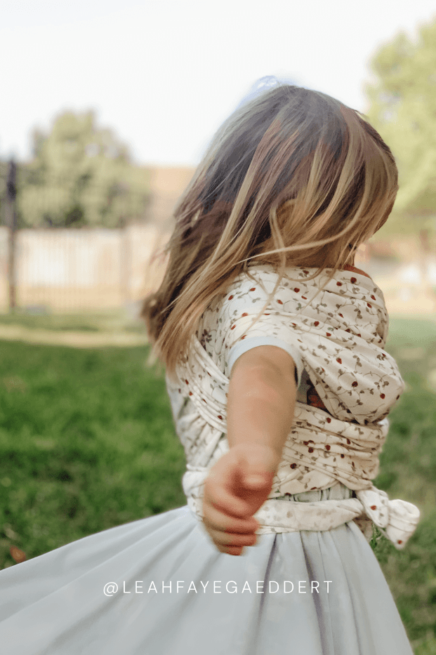 Child wearing a floral dress outdoors wearing strawberry solly dolly wrap for play.
