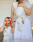 Woman holding a baby in strawberry baby wrap carrier and a young girl taking a photo with a red camera, carrying her doll in a solly baby solly dolly play carrier.