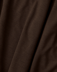 A close-up of dark brown textured fabric with soft folds and a fine woven pattern.