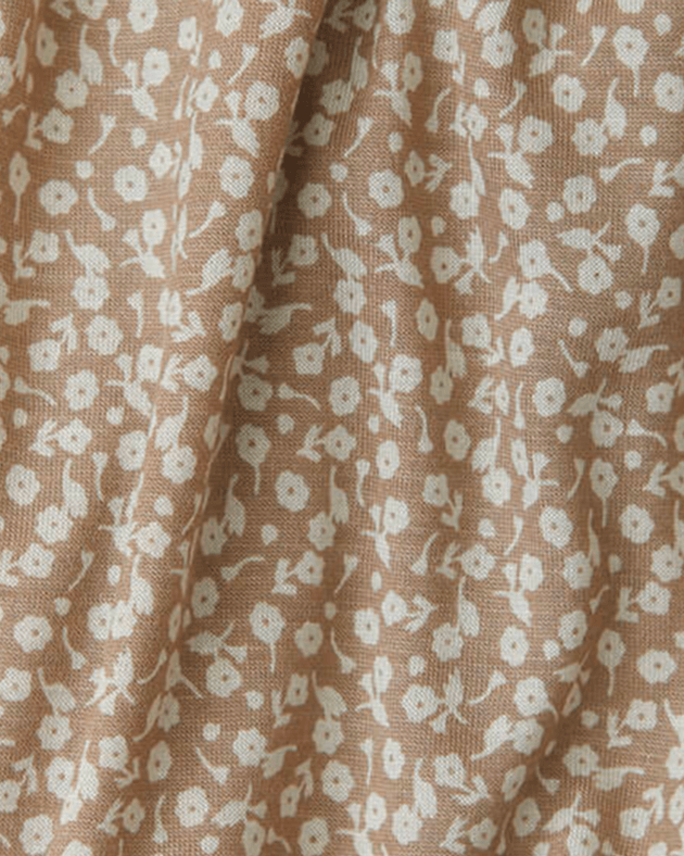 A close-up of a woven fabric with a small-scale floral pattern in off-white on a warm tan background.
