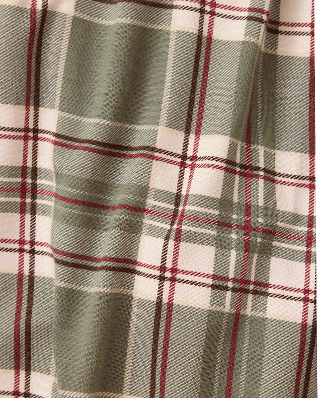 A close-up of a plaid fabric pattern with a muted sage green base, cream blocks, and thin red and black stripes.