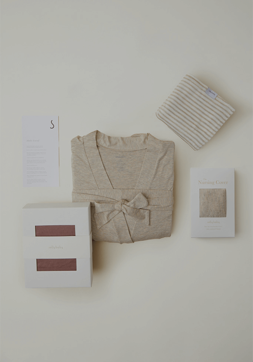 A thoughtfully curated collection of baby shower gifts is displayed against a neutral background. The set includes a soft beige robe tied with a bow, a striped baby blanket, and two neatly packaged Solly Baby Wraps in muted tones, offering warmth and comfort for parents and little ones alike.