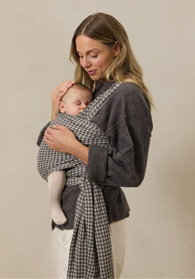 A mother standing while holding her baby in a Stormy Houndstooth Solly Baby Wrap.