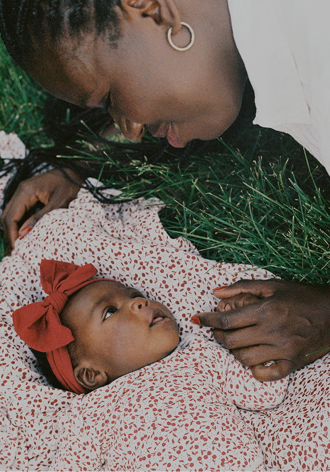 Close-up of mother and baby resting in the grass, baby in Solly Baby Cherry print. A quiet, connected moment full of tenderness and love.