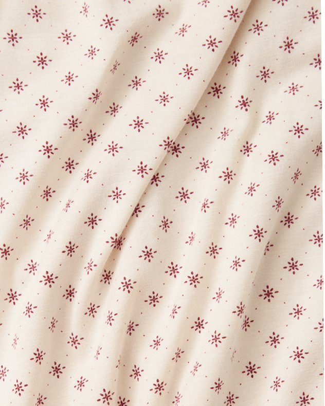 A close-up of a cream-colored fabric with a repeating pattern of small red star or snowflake-like motifs, shown with soft folds.