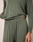 A close-up of a person wearing a matching two-piece lounge set in olive green, featuring a long-sleeve top and high-waisted pants with an elastic waistband.