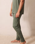 A person wearing a matching two-piece lounge set in olive green, featuring a short-sleeve crewneck t-shirt and slim-fit pants, standing barefoot against a neutral beige wall.