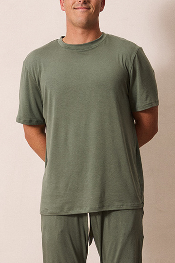 A man wearing a matching olive green short-sleeve t-shirt and sweatpants set, standing against a plain beige background.