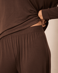 Close-up of a person wearing a dark brown long-sleeve top and matching dark brown lounge pants, lifting the hem of the top to show the elastic waistband.