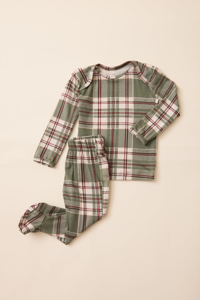A two-piece baby pajama set featuring a long-sleeve top and matching footed pants in an olive green plaid pattern with red and white stripes, laid flat on a light beige background.