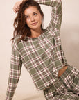 A woman wearing a green plaid long-sleeve top and matching pants, posing against a neutral beige background.