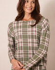 A woman wearing a long-sleeve plaid top in sage green, pink, and white, standing against a plain beige background.