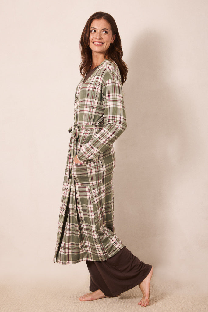 A woman modeling a long-sleeve green plaid robe with a tie waist, paired with dark brown pants, standing against a plain beige studio background.