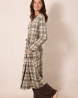 A woman modeling a long-sleeve green plaid robe with a tie waist, paired with dark brown pants, standing against a plain beige studio background.
