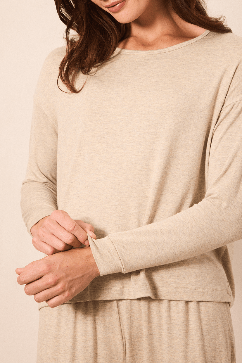 A woman wearing a light beige long-sleeve knit top and matching bottoms, shown from the shoulders to the hips against a plain warm beige background.