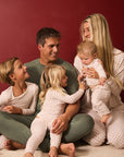 A family of five wearing matching light red and white twinkle star pajamas sits together on a cream carpet against a solid dark red background.