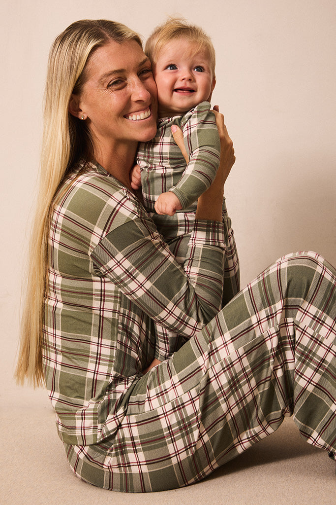 A smiling woman and a young child wearing matching green plaid pajamas, posed together against a plain beige studio background.