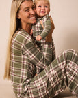 A smiling woman and a young child wearing matching green plaid pajamas, posed together against a plain beige studio background.