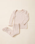 A two-piece baby pajama set featuring a long-sleeve top and matching footed pants, both in a light cream fabric with a small red star pattern, laid flat on a warm beige background.