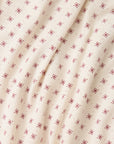 A close-up of a cream-colored fabric with a repeating pattern of small red star or snowflake-like motifs, shown with soft folds.