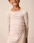 A smiling young boy wearing a long-sleeve pajama top and matching pants set in a cream color with a small red star pattern, set against a plain beige background.