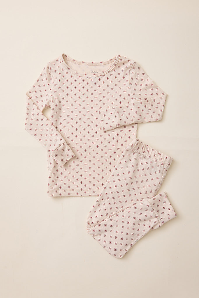 A two-piece baby pajama set featuring a long-sleeve top and matching pants in a soft cream fabric with a small red star pattern, laid flat on a light beige background.