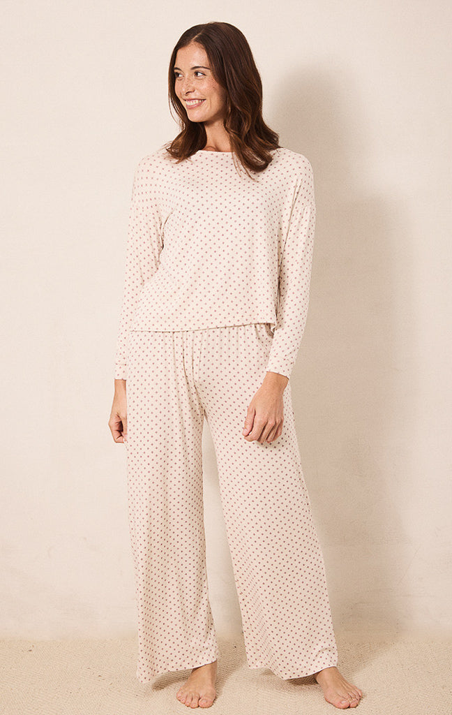 A woman modeling a two-piece long-sleeve pajama set with a small red star pattern on a cream background, standing against a neutral beige backdrop.
