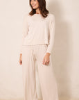 A woman modeling a two-piece long-sleeve pajama set with a small red star pattern on a cream background, standing against a neutral beige backdrop.