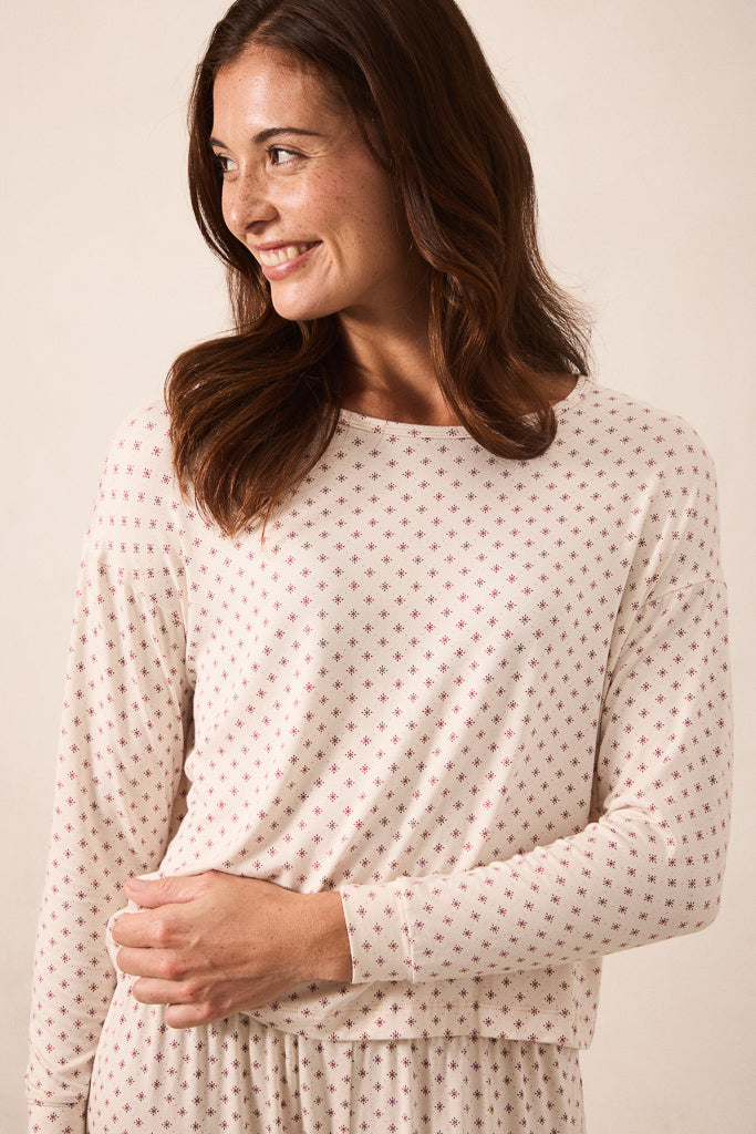 A woman wearing a cream-colored long-sleeve top with a small red star pattern, photographed against a solid light beige background.
