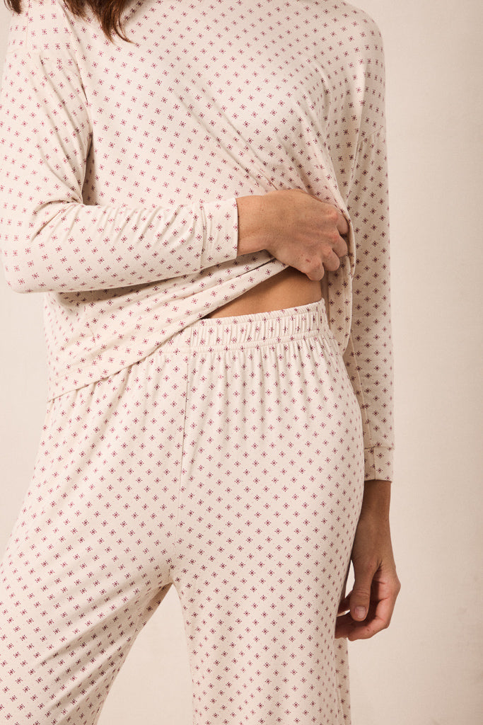 A person wearing a matching long-sleeve top and pants pajama set in a light cream color with a small repeating red star pattern, shown against a plain beige background.
