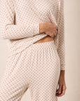 A person wearing a matching long-sleeve top and pants pajama set in a light cream color with a small repeating red star pattern, shown against a plain beige background.