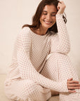 A woman sitting on a textured beige floor wearing a matching long-sleeve pajama set with a small red star pattern on a cream background.