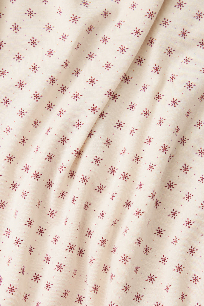 A close-up of a cream-colored fabric with a repeating pattern of small red star or snowflake-like motifs, shown with soft folds.
