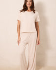 A woman modeling a two-piece pajama set consisting of a short-sleeve top and matching wide-leg pants, both in a light beige color with a small red star pattern, set against a plain beige studio background.