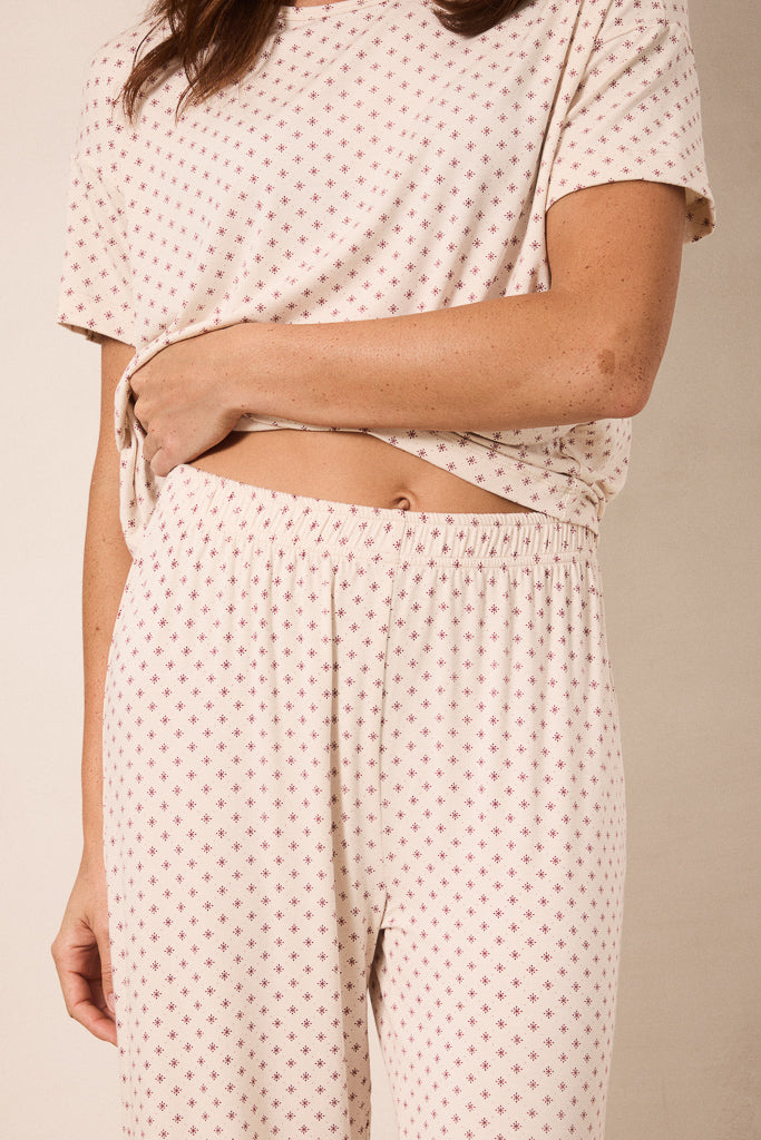 A close-up of a person wearing a matching two-piece loungewear set with a short-sleeve top and wide-leg pants, both in a light cream fabric with a small red star pattern.