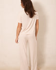 A woman shown from the back wearing a matching short-sleeve top and wide-leg pants pajama set in a warm cream color with a small red star pattern, standing against a plain beige wall.