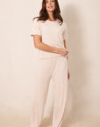 A woman modeling a matching two-piece loungewear set consisting of a short-sleeve top and wide-leg pants, both in a light cream color with a small red star pattern, against a plain beige studio background.