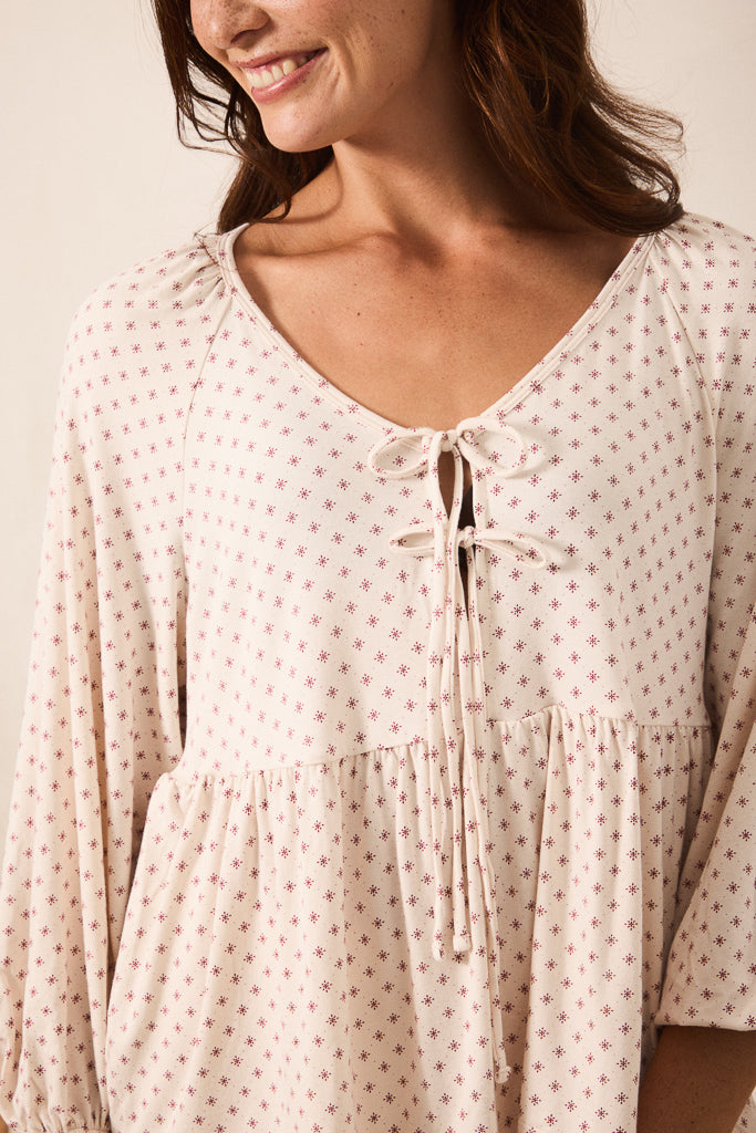 A close-up of a woman wearing a cream-colored long-sleeve blouse with a small red star pattern and a tie-front neckline.